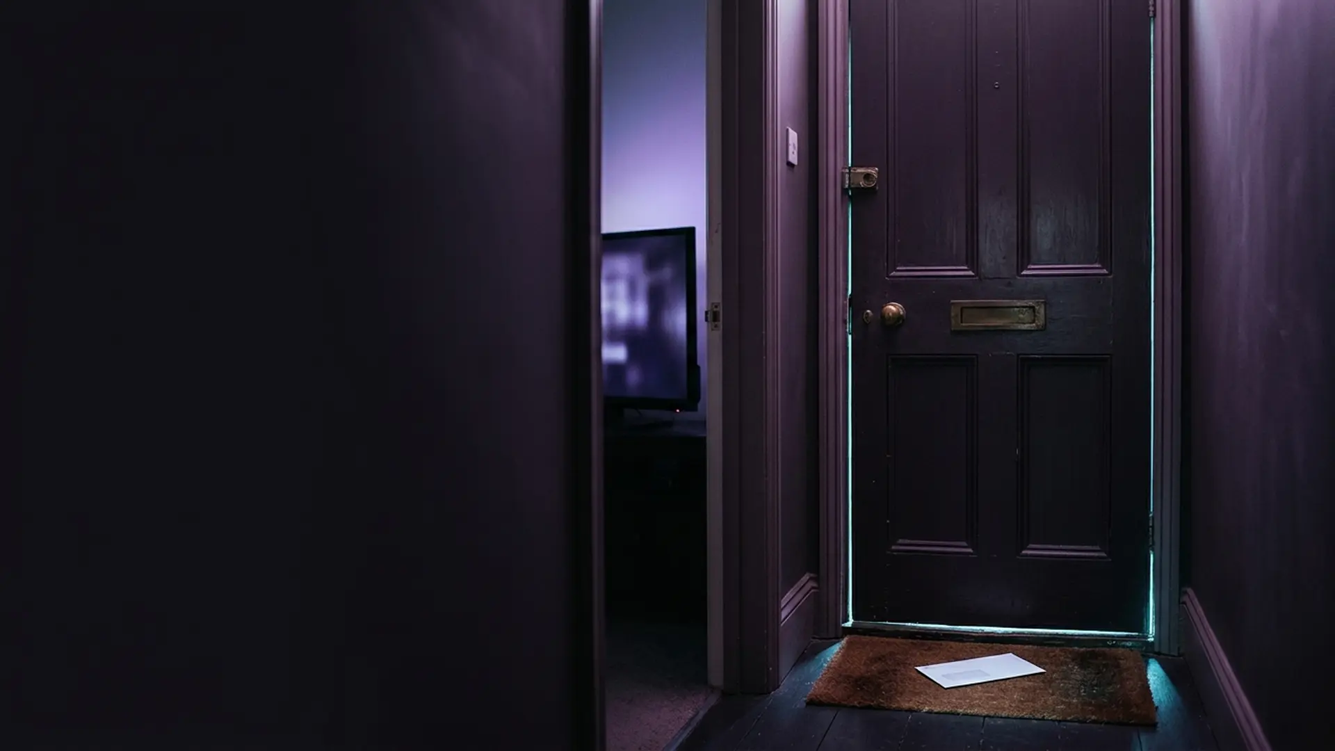 An official envelope on a doormat with television light from the lounge